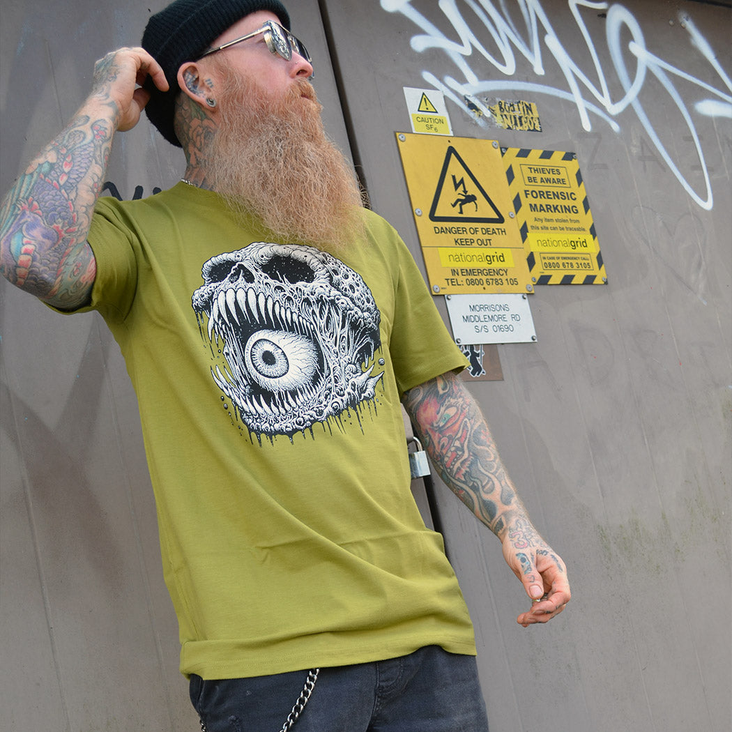 Man wearing a green t-shirt with a skull illustration, standing in front of a door.