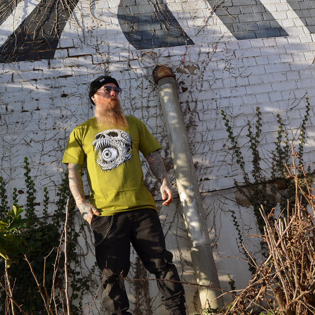 Man wearing a green t-shirt with a skull illustration, standing in front of a wall.