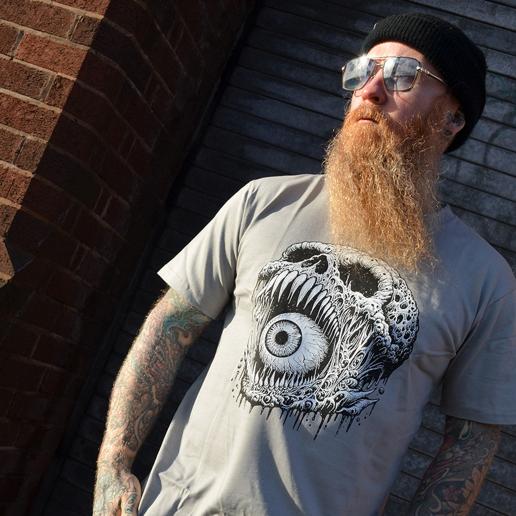 Man wearing a t-shirt with a black and white eye skull design against a brick wall.