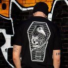 Person wearing a black t-shirt with a white graphic design on the back, standing in front of a graffiti-covered wall.