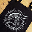 Black tote bag with white alien design on a wooden surface