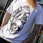 Person wearing a white t-shirt with a black graphic design, standing against a metal fence.