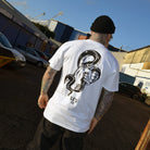 Person wearing a white t-shirt with a black snake illustration outdoors.