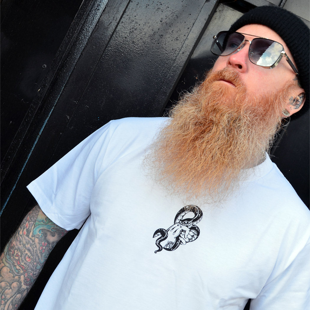 Man with a long beard and tattoos wearing a white t-shirt with a snake illustration.